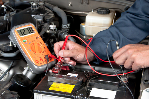 An auto mechanic uses a multimeter voltmeter to check the voltage level in a car battery.